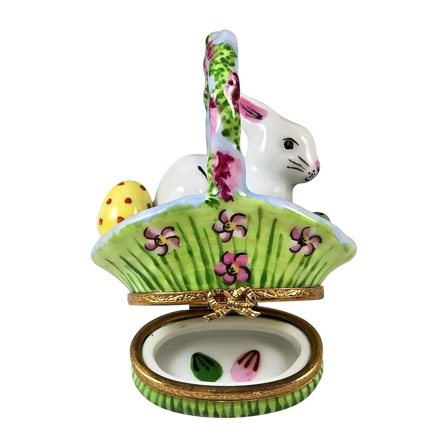 White rabbit figurine with long ears and pink nose sitting in a colorful Easter basket surrounded by wisteria flowers and greenery Limoges box